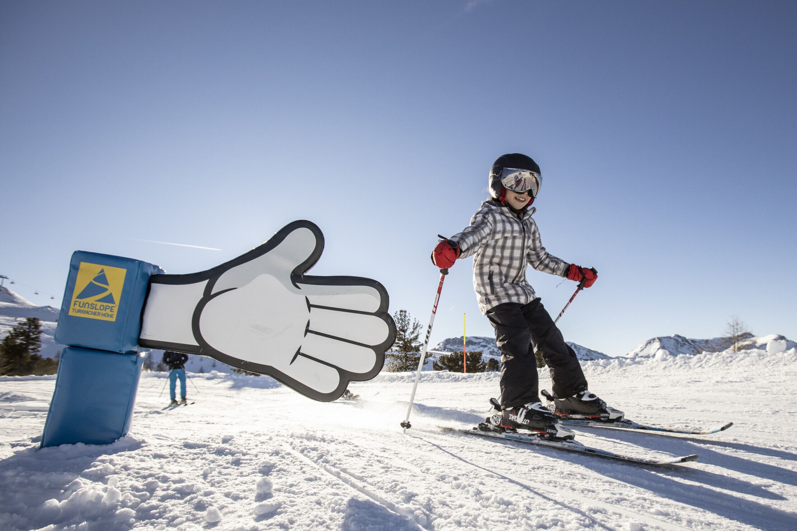 Eine Person fährt auf einem mit Schnee bedeckten Hang, in der Nähe steht ein großes, handgefertigtes Schild.