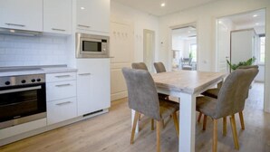 Una cocina moderna con armarios blancos, horno empotrado, microondas y una mesa de comedor de madera con cuatro sillas.