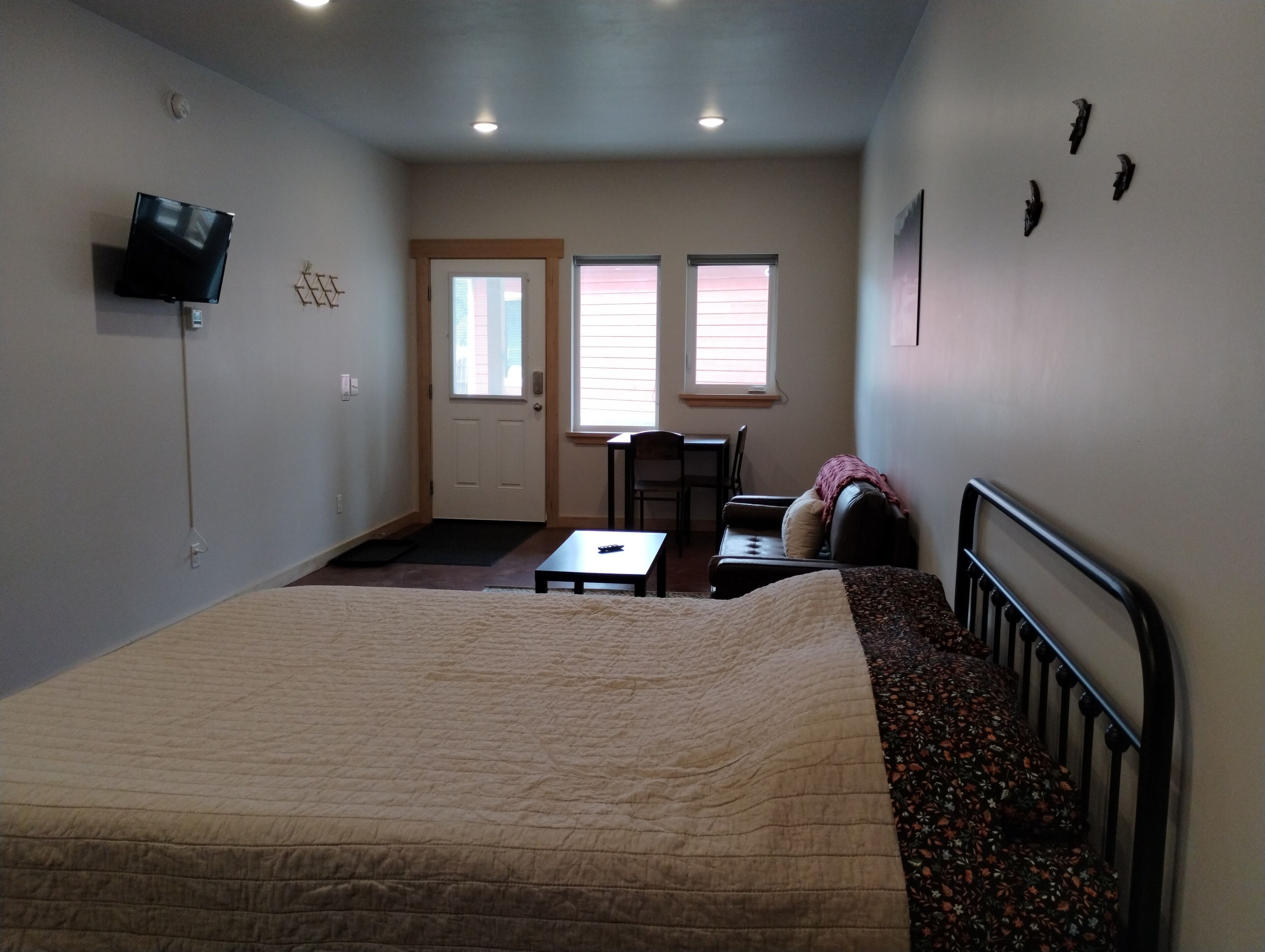 A bedroom with a bed, a desk, a chair, and a TV on the wall.