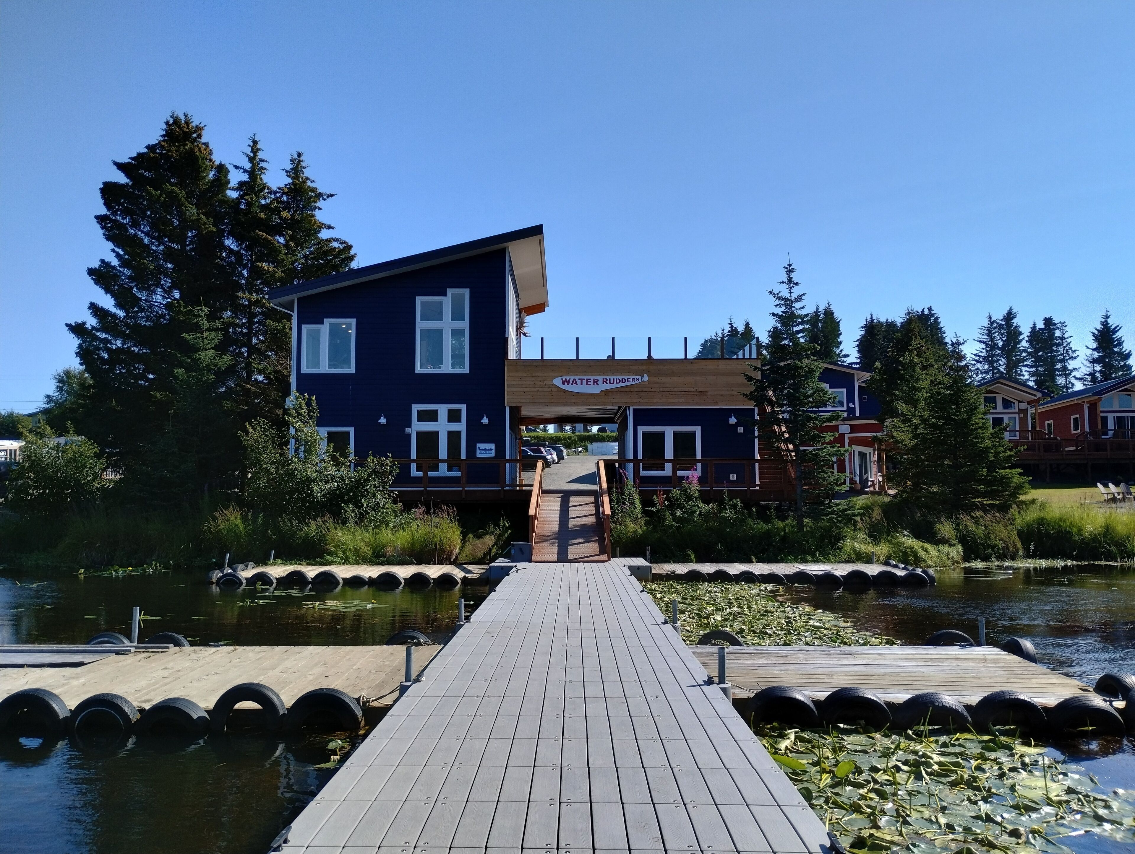 A wooden dock leading to a blue building with a sign reading "WATER RUDDERS". - Grewingk Suite - Homer Seaplane Base (Homer)