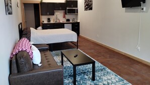 A compact living space with a bed, a sofa, a small table, and a kitchenette. - Grewingk Suite - Homer Seaplane Base (Homer)