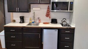 A compact kitchen with dark cabinets, a stainless steel microwave, a coffee maker, a toaster, and a kettle. - Grewingk Suite - Homer Seaplane Base (Homer)