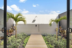 Un sendero conduce a un edificio blanco con un panel solar en el techo, rodeado de plantas y palmeras.