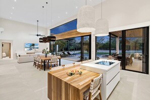 Une cuisine moderne dotée d’un îlot central, d’un coin repas et de grandes fenêtres offrant une vue sur l’extérieur.