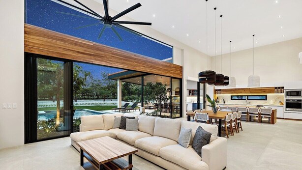 Un salon moderne avec un canapé d’angle, une table basse et une vue sur une piscine et un espace de détente extérieur.