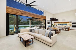 A modern living room with a sectional sofa, a coffee table, and a view of a pool and outdoor seating area. - Casa Maui (Reserva de Golf, Hacienda Pinilla)