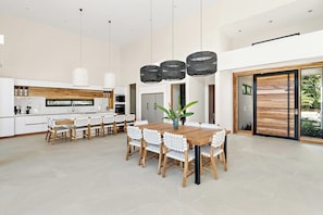 Una cocina amplia con comedor, que cuenta con una gran mesa de madera y sillas, luces colgantes y vistas por un puerta corrediza de vidrio.