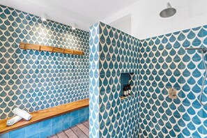 A bathroom with a blue and white leaf pattern tile design, a wooden bench, and a shower area.