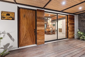 A modern interior with a wooden floor, a dining area with a table and chairs, and a kitchen visible through a glass door.