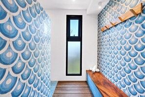 A narrow hallway with a patterned blue and white wall design, a wooden bench, and a small window.