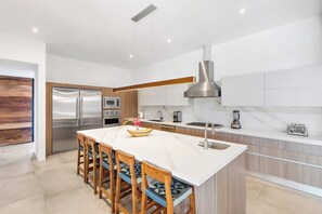 A modern kitchen with a central island, stainless steel appliances, and a wooden dining area.