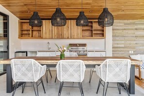 A modern kitchen with a wooden countertop, white woven chairs, and black pendant lights.