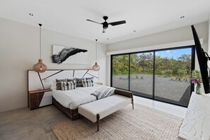 A modern bedroom with a large bed, a ceiling fan, and a view of a garden through large windows.