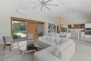 A modern living room with a large sectional sofa, a coffee table, and a dining area with a wooden table and chairs.