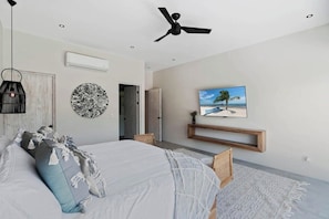 A modern bedroom with a bed, a ceiling fan, a TV, and a wall-mounted shelf.