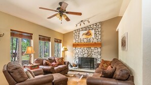 A living room with leather sofas, a stone fireplace, and a ceiling fan. - Pet-friendly cabin in the pines, 2 decks w/grill, <10 to skiing (Angel Fire)