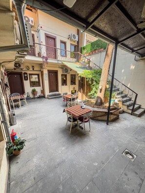 A courtyard with a table and chairs, a fire extinguisher, and a staircase leading to an upper level.