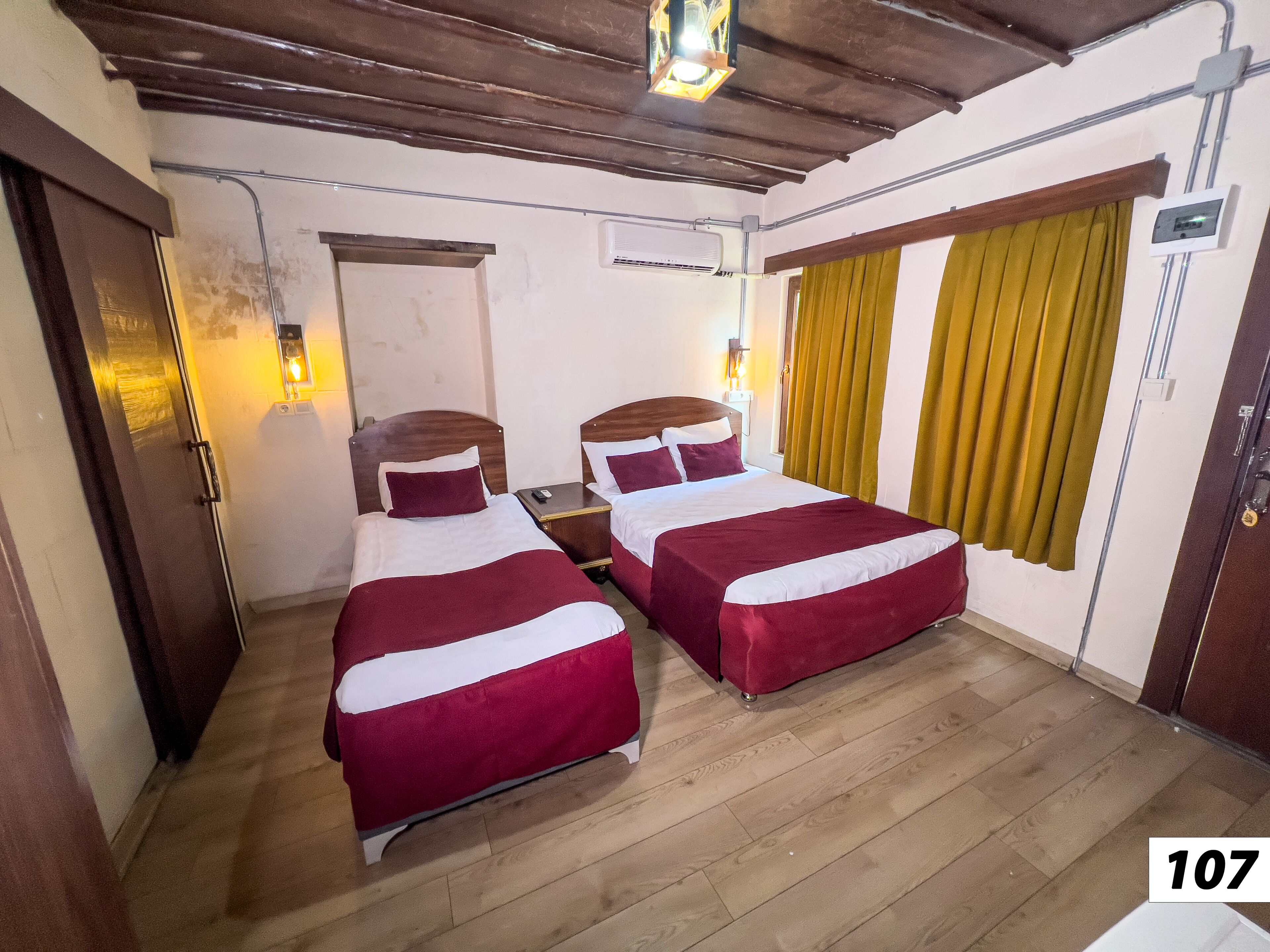 Une chambre avec deux lits, un plancher en bois, un ventilateur de plafond et une fenêtre avec des rideaux.