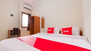 Une chambre d’hôtel avec un lit, deux oreillers rouges ornés du mot « OYO », une armoire en bois, un bureau avec une chaise et une fenêtre donnant sur un paysage.