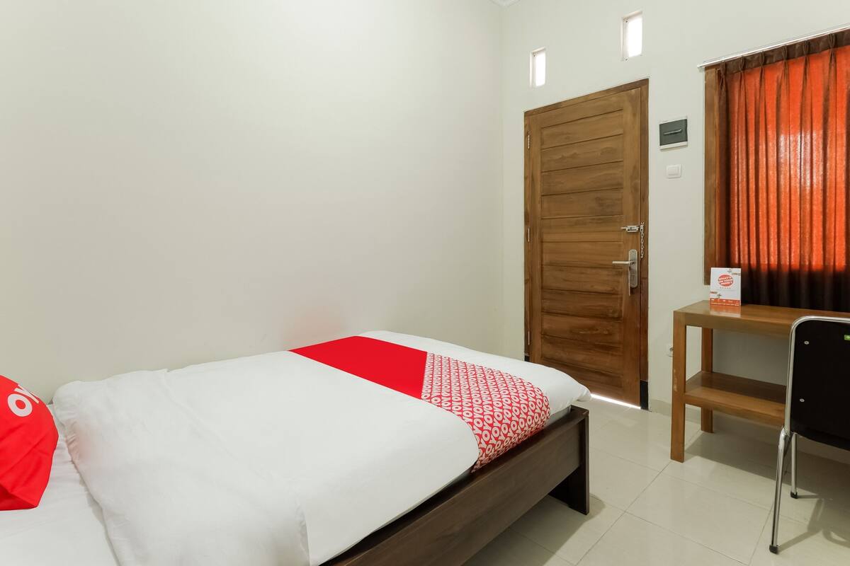 A bedroom with a bed, a wooden door, a desk, and a chair.