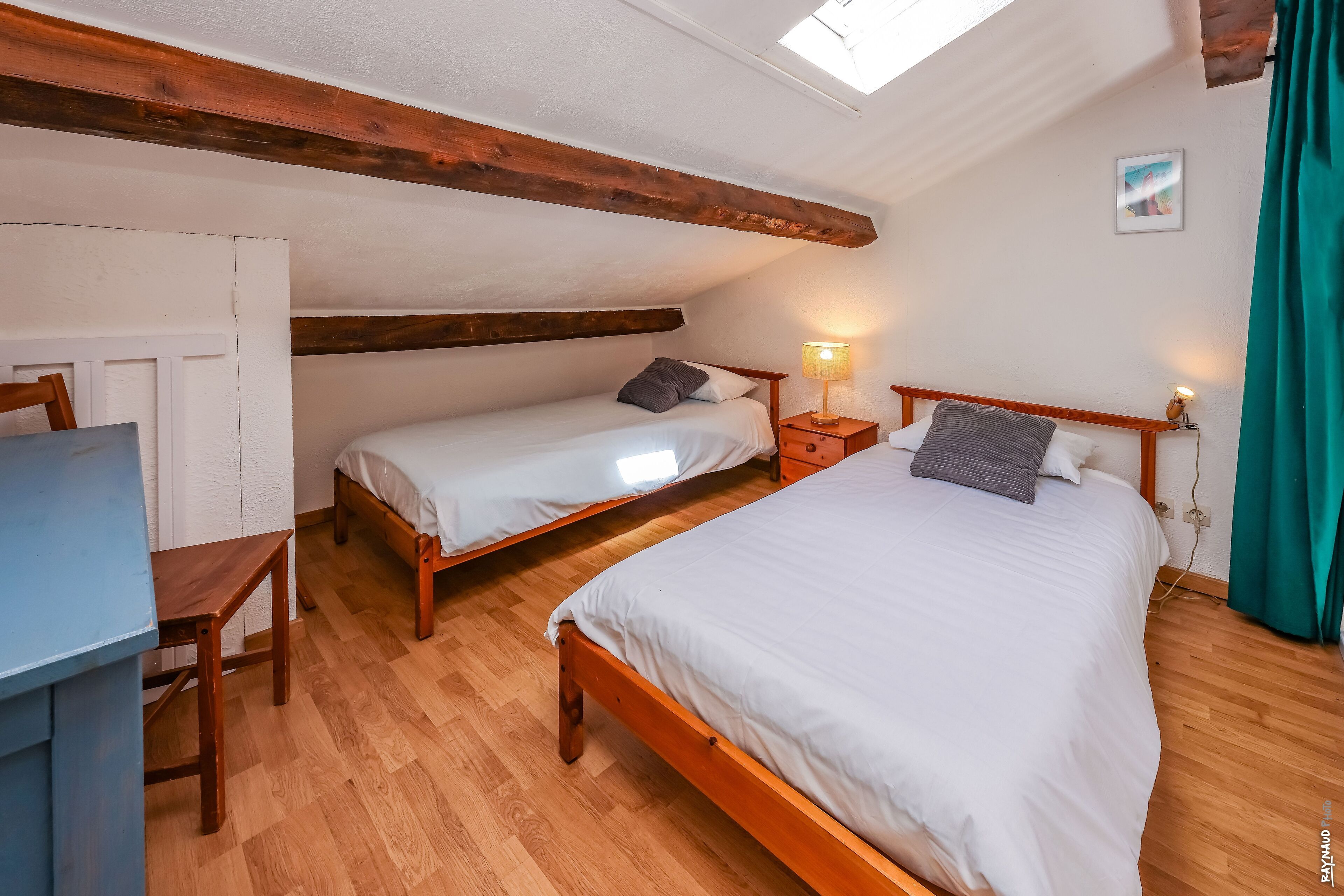 A cozy bedroom with two wooden beds, a desk, and a skylight.