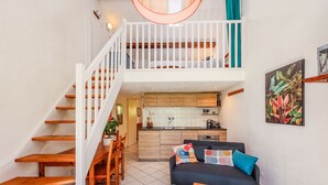 Un vaste espace de vie agrémenté d’un canapé bleu foncé, d’une table basse en bois et d’un escalier menant à une chambre située en mezzanine.