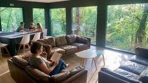 Un intérieur moderne avec un canapé en cuir, une table à manger et de grandes fenêtres donnant sur un paysage verdoyant.