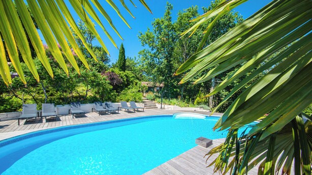 Une piscine dotée d’une terrasse en bois et de chaises longues, entourée d’une végétation luxuriante et d’arbres.