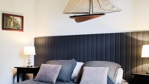 Habitació d'hotel moderna amb un llit gran, un panell frontal amb línies verticals, dues taules de nit amb làmpades i una decoració de veler sobre el llit.