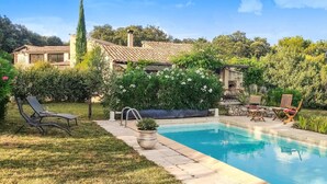 Una piscina amb un terrat de pedra, envoltada per un jardí amb diverses plantes i una zona de pati amb mobiliari exterior.