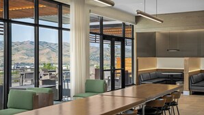 A modern lounge area with a long wooden table, green and black seating, and large windows offering a mountain view. - Courtyard BY Marriott Pocatello (Pocatello)