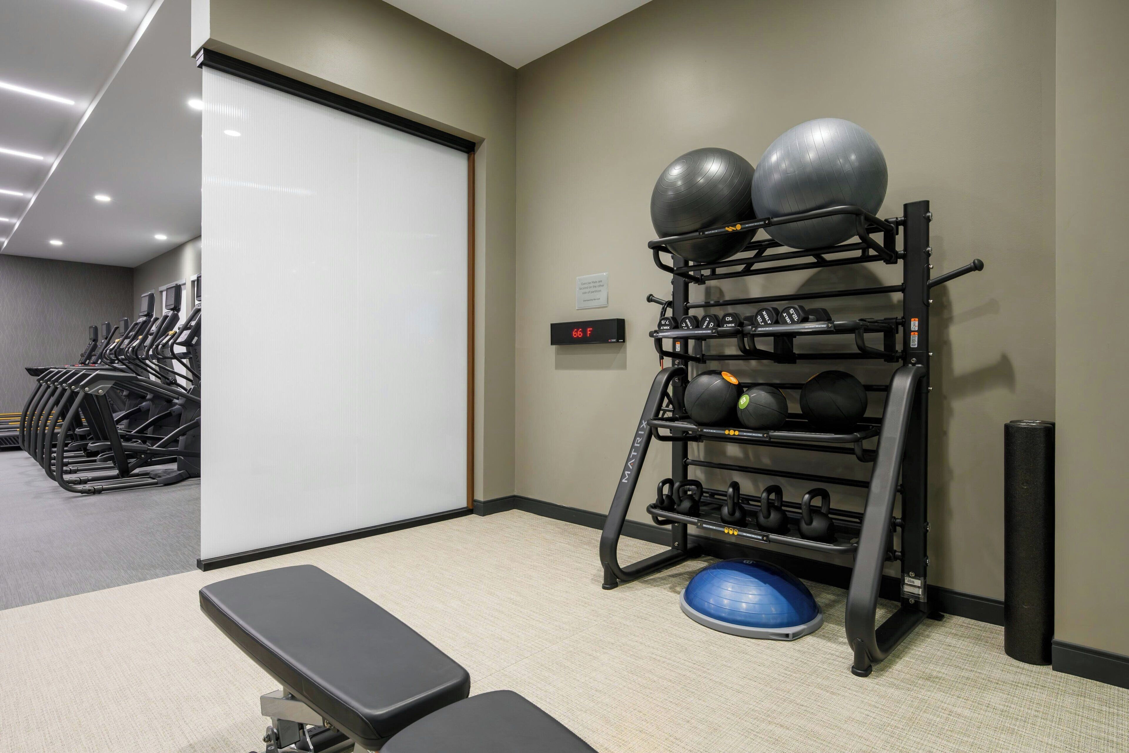 A gym with treadmills, a bench, a rack with exercise balls and weights, and a digital display.