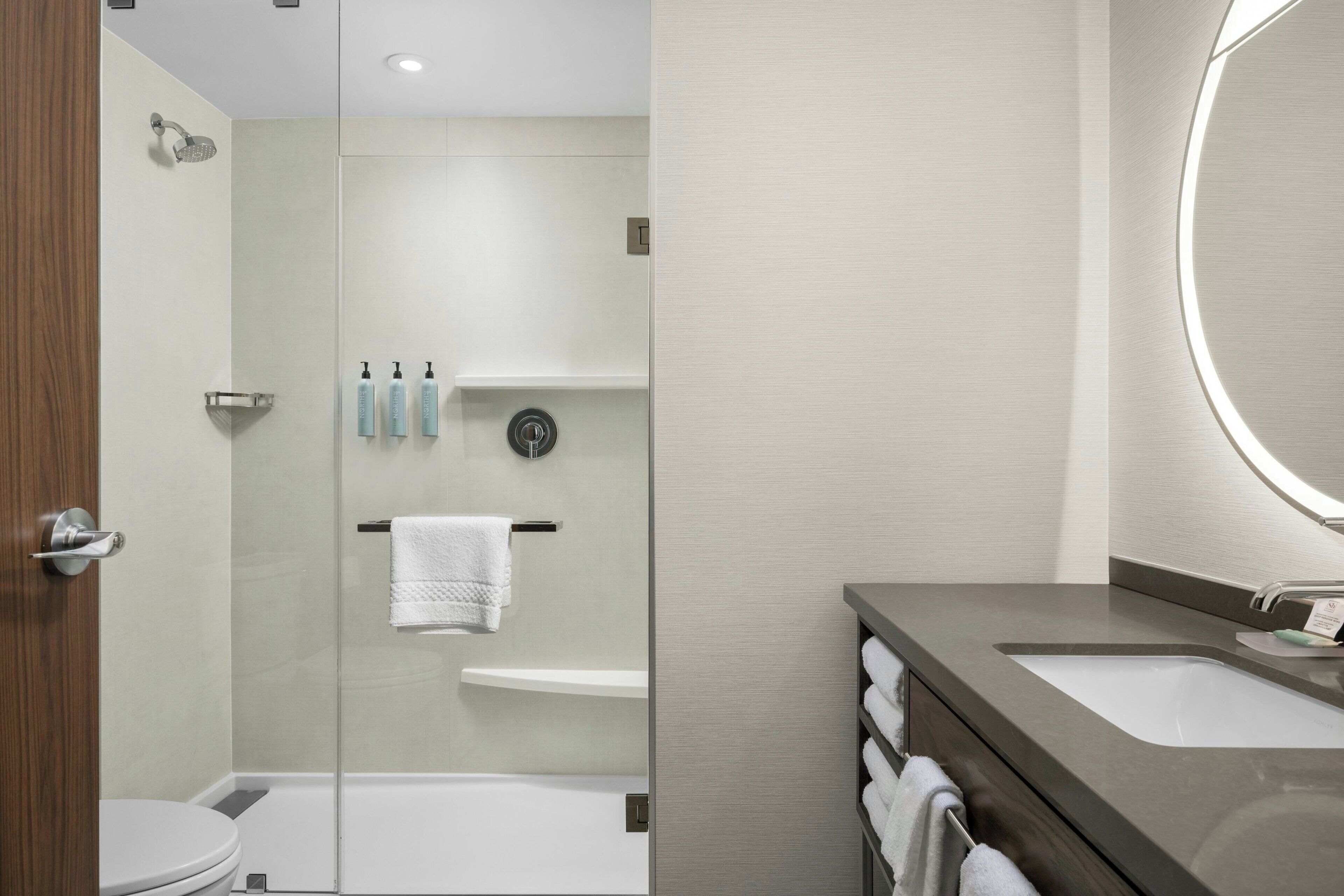 A modern bathroom with a glass shower enclosure, a white toilet, a sink with a mirror, and a towel rack with folded towels.