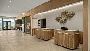 A modern reception area with wooden reception desks, a wall-mounted abstract art piece, and a view of the outdoors through large windows. - Courtyard BY Marriott Pocatello (Pocatello)