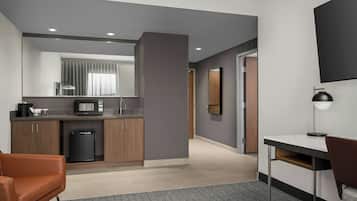 A modern hotel room with a kitchenette, a desk, a chair, and a large mirror.