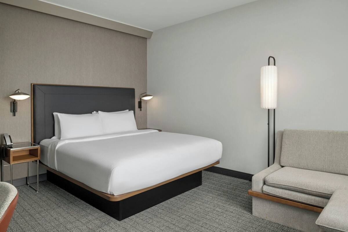A modern hotel room with a large bed, bedside tables, a chair, and a floor lamp.
