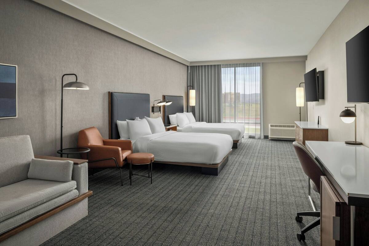 A hotel room with two beds, a sofa, a desk, and a TV.