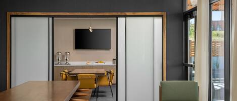 A modern conference room with a long table, yellow chairs, a green armchair, and a TV mounted on a dark wall.