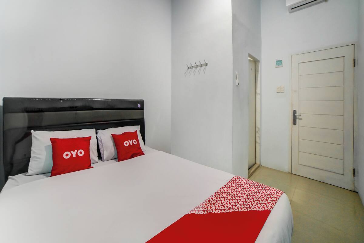 A hotel room with a bed, a red and white bedspread, a black headboard, and a white door.