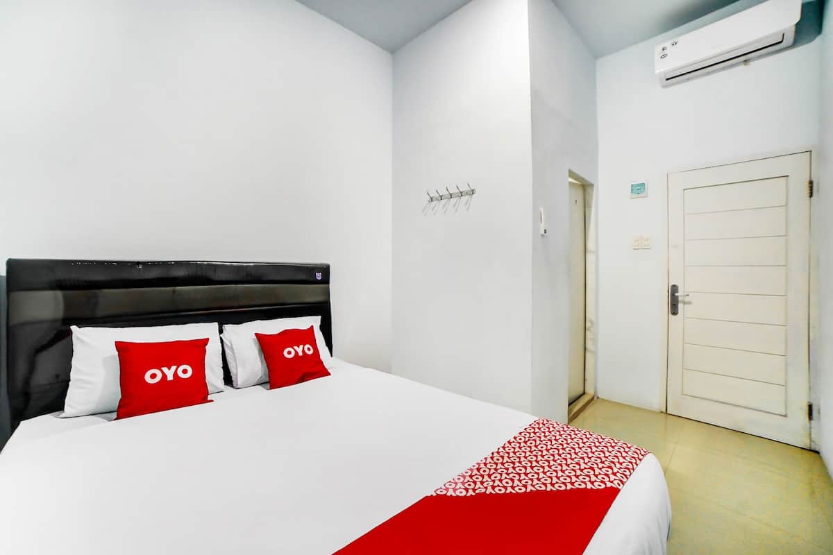 A hotel room with a bed, a white wall, a door, and an air conditioning unit.