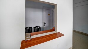 A reception area with a wooden counter, a door with a sign, and two black trash bins. - Hotel O Ada Guest House (Medan)