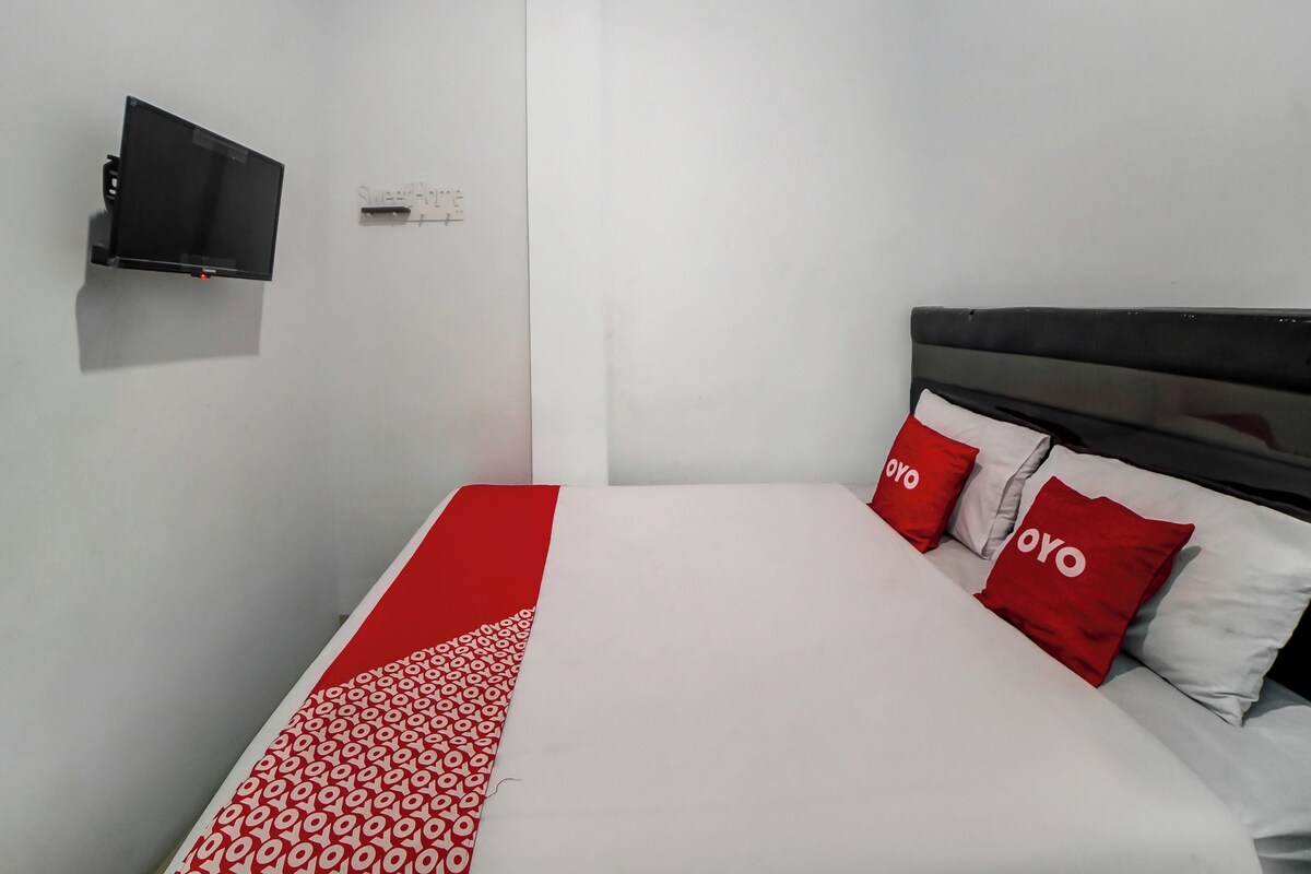 Ein Hotelzimmer mit Bett, Wandfernseher und zwei roten Kissen mit 'OYO'-Branding.