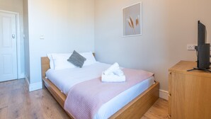 A bedroom with a bed, a wooden nightstand, a television, and a framed picture on the wall.