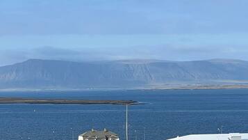 A coastal view with a large mountain in the background, a white building with a green lawn in the foreground, and a modern white building with a flat roof.