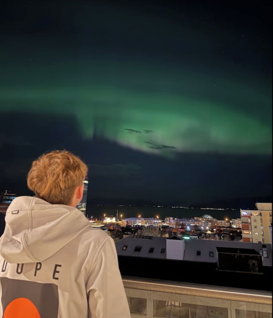 A person standing on a balcony overlooking a cityscape with buildings and a view of the night sky.