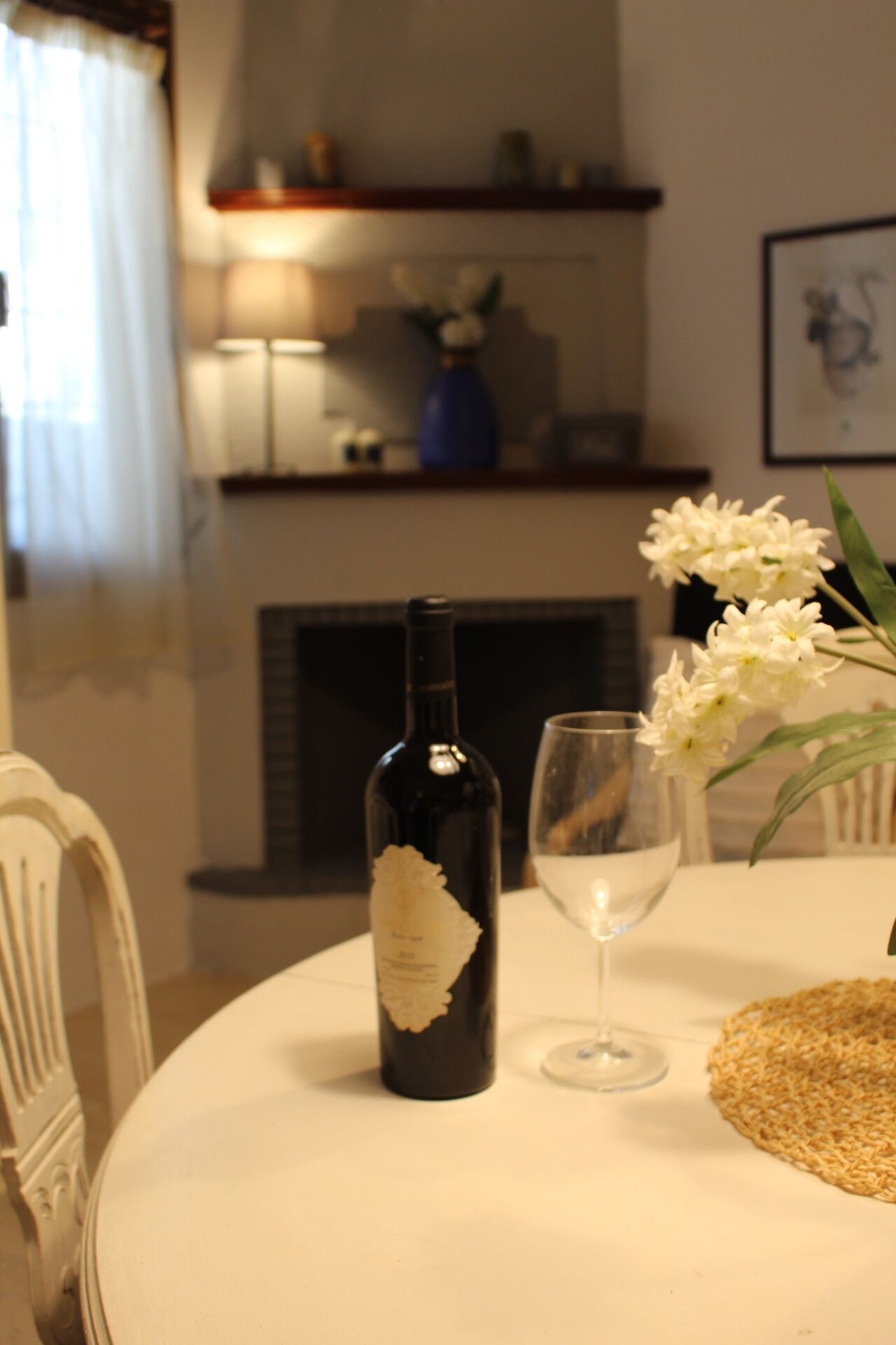 Una mesa de comedor con una botella de vino, una copa y un florero con flores.