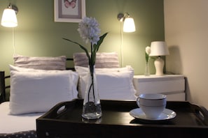 A hotel room with a bed, two bedside lamps, a vase with flowers, and a tray with a cup and saucer. - GVA House (Skiathos)