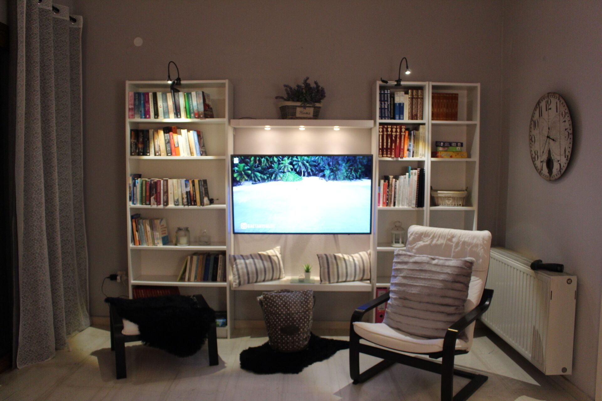 A living room with a large flat-screen TV, a bookshelf, a chair, and a radiator.