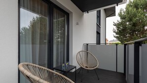 A balcony with two wicker chairs, a small table with drinks, and a glass door leading to a room. - Cozy Apartment | Close to Beach and Lake, Parking. (Mielno)