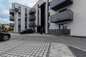 A modern building with balconies, a paved entrance, and a car parked in front.